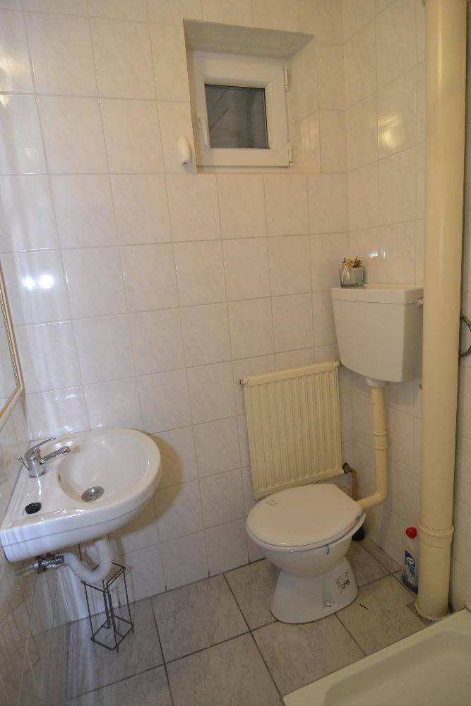 Einfaches Badezimmer mit Badewanne, Waschbecken und kleinem Fenster.