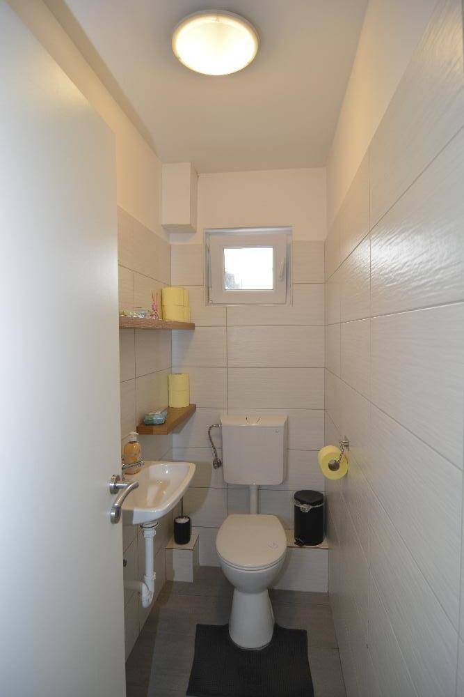 Kleines Gäste-WC mit Waschbecken, Toilette und Fenster für Belüftung.