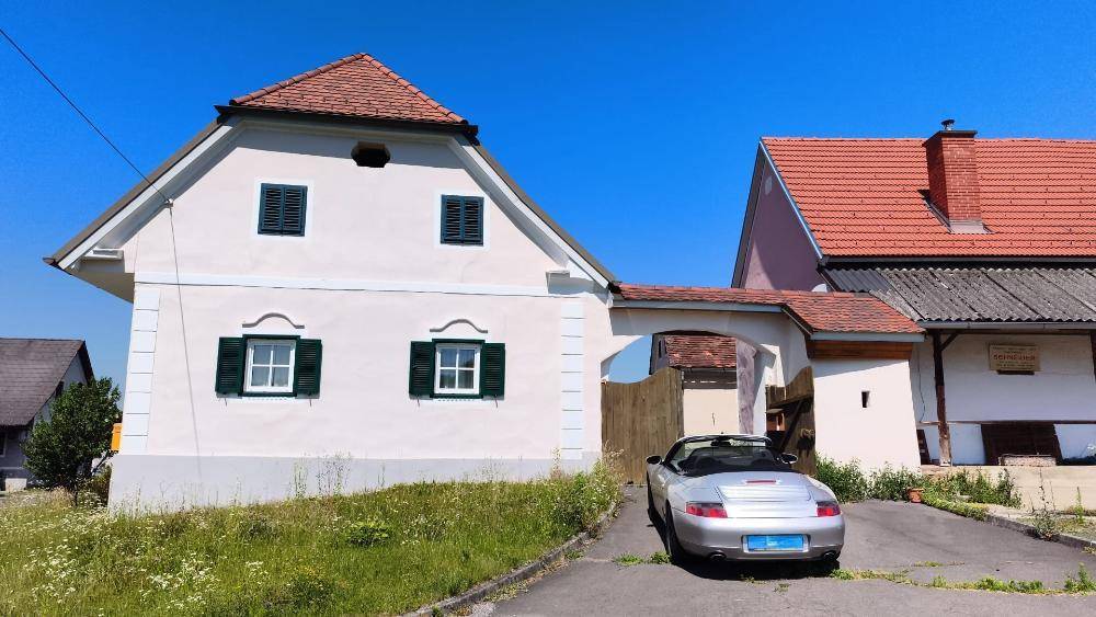 Ansicht eines traditionellen Landhauses mit rotem Dach und einem geparkten Sportwagen davor.