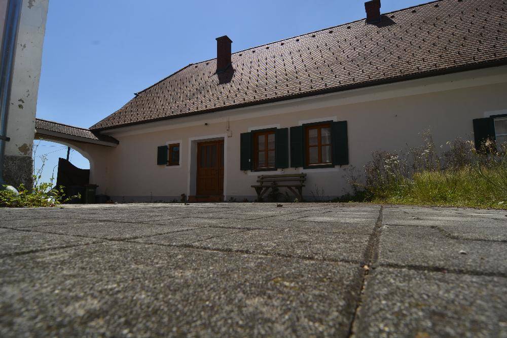 Eingangsbereich eines traditionellen Hauses mit Holztür, grünen Fensterläden und gepflastertem Boden.
