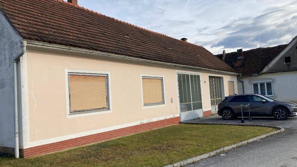 Ländliches Gebäude mit beiger Fassade, Ziegeldach und einem geparkten Auto davor.