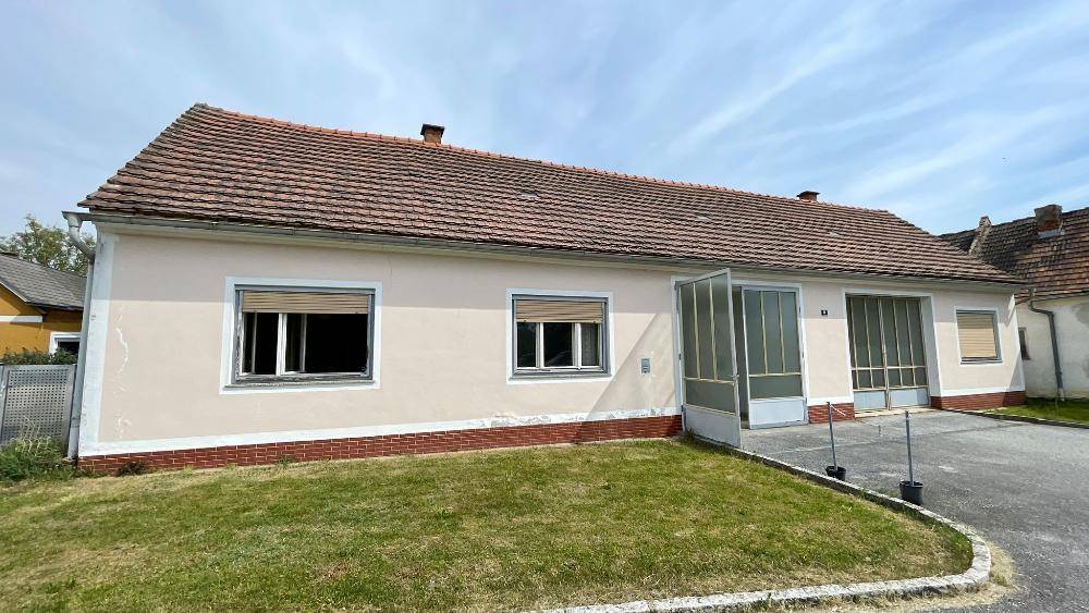 Ländliches Haus mit beiger Fassade, Ziegeldach und geschlossenen Fensterläden.