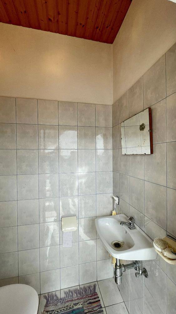 Kleines WC mit Waschbecken, hellgrauen Fliesen und Holzdecke, einfach und praktisch.