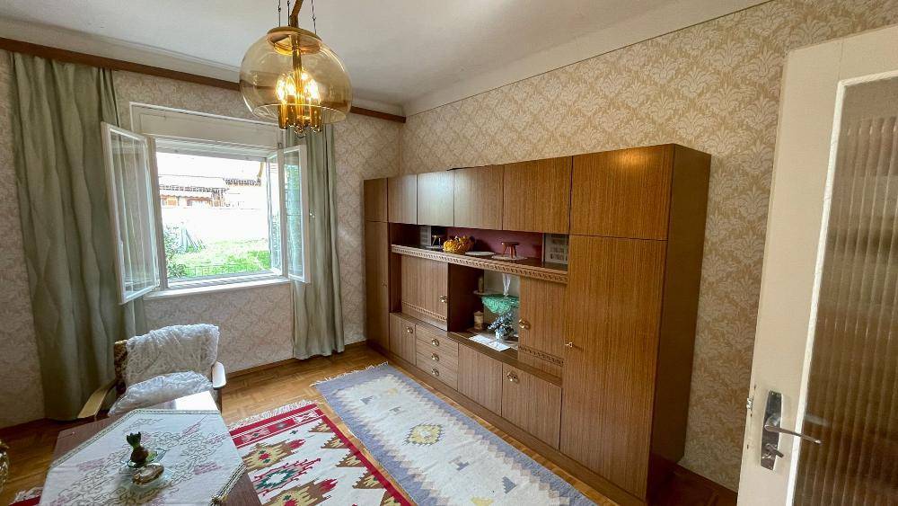 Wohnzimmer im Vintage-Stil mit Holzschrankwand, Teppich und Blick ins Grüne.