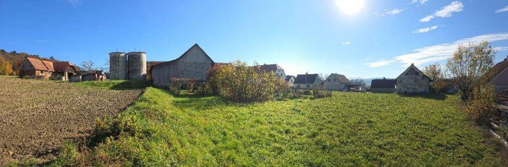 Weitläufige ländliche Landschaft mit Feldern, Wiesen und traditionellen Bauernhäusern unter blauem Himmel.