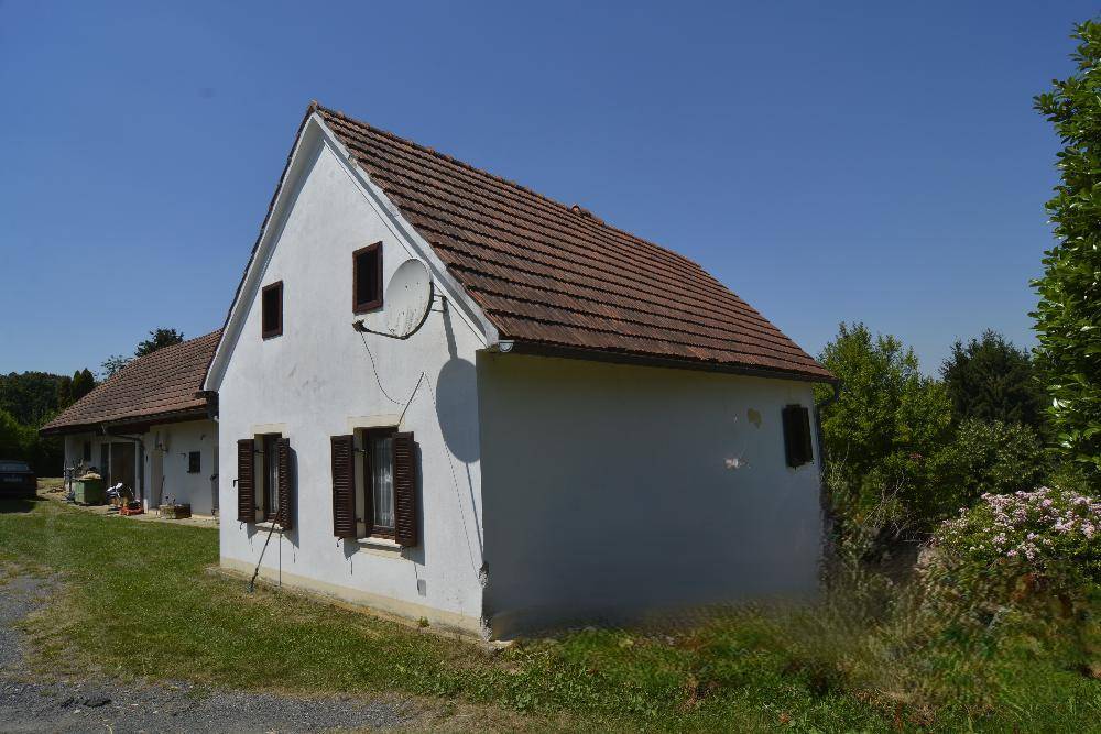 Vorderansicht des weißen Landhauses mit braunen Fensterläden und rotem Ziegeldach an einem klaren Tag.