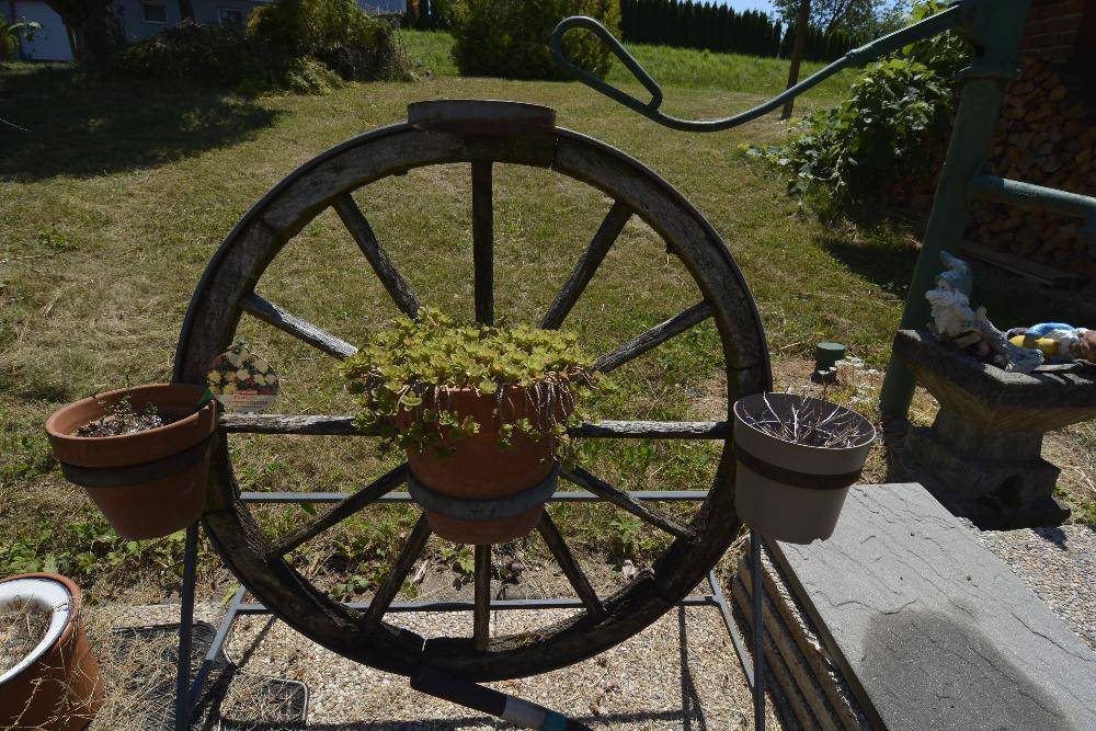 Dekoriertes Wagenrad mit Topfpflanzen und Gartenzwergen als charmante Gartendekoration.