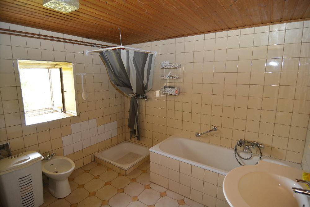 Traditionelles Badezimmer mit beigen Fliesen, Badewanne, Dusche, Bidet und Holzdecke.