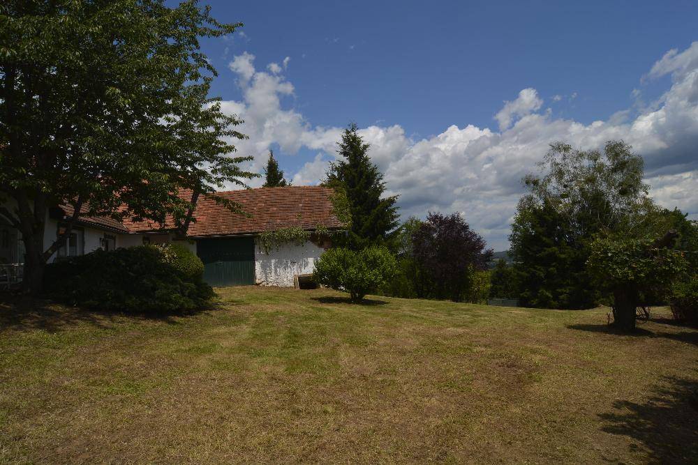 Weitläufiges Grundstück mit ländlichem Haus, grüner Wiese und Bäumen unter bewölktem Himmel.