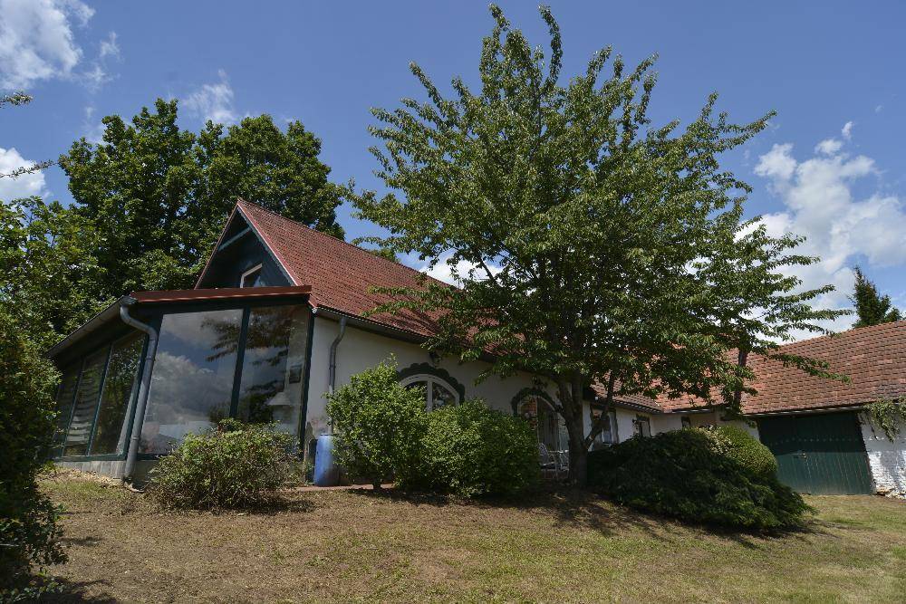 Charmantes Landhaus mit Wintergarten und üppiger Vegetation unter blauem Himmel.