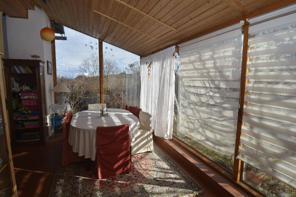 Heller Wintergarten mit Esstisch, großen Fenstern und Blick ins Grüne.