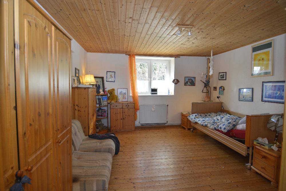 Gemütliches Schlafzimmer mit Holzvertäfelung an der Decke und Holzdielenboden.