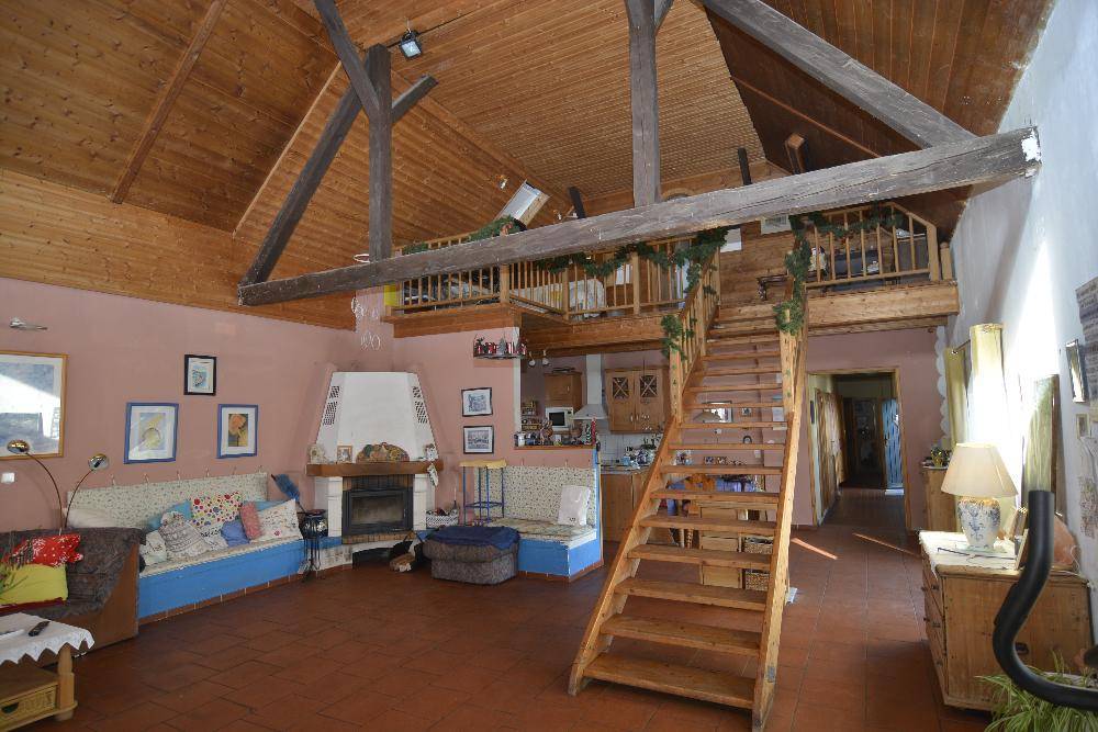 Geräumiges Wohnzimmer mit hohen Holzdecken, sichtbaren Balken, Kamin und Holztreppe zur Galerie.