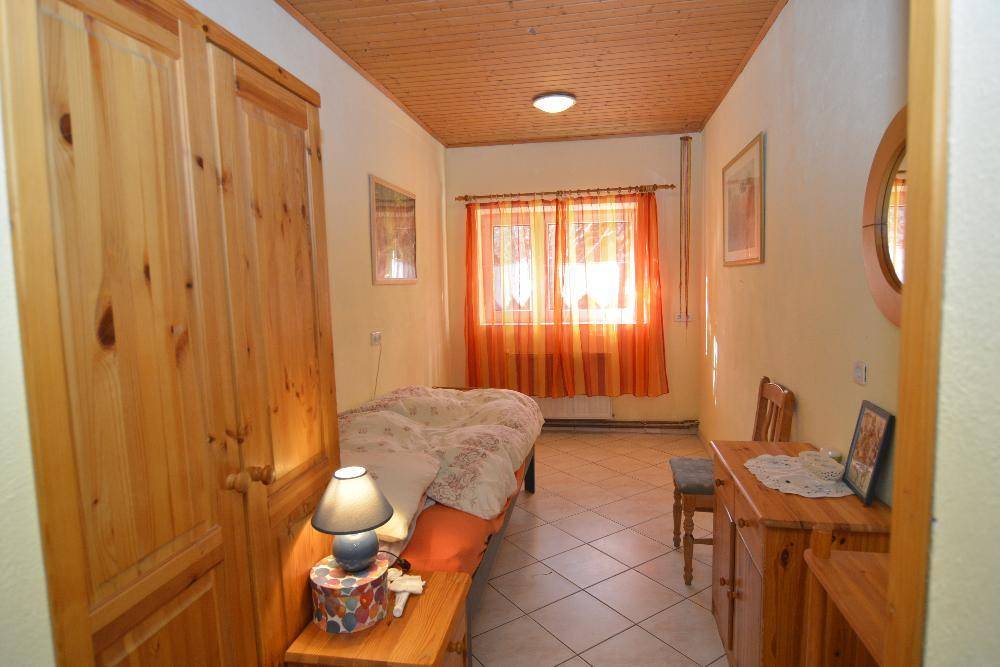 Helles Schlafzimmer mit Holzschrank, Einzelbett und Fenster mit orangefarbenen Vorhängen.