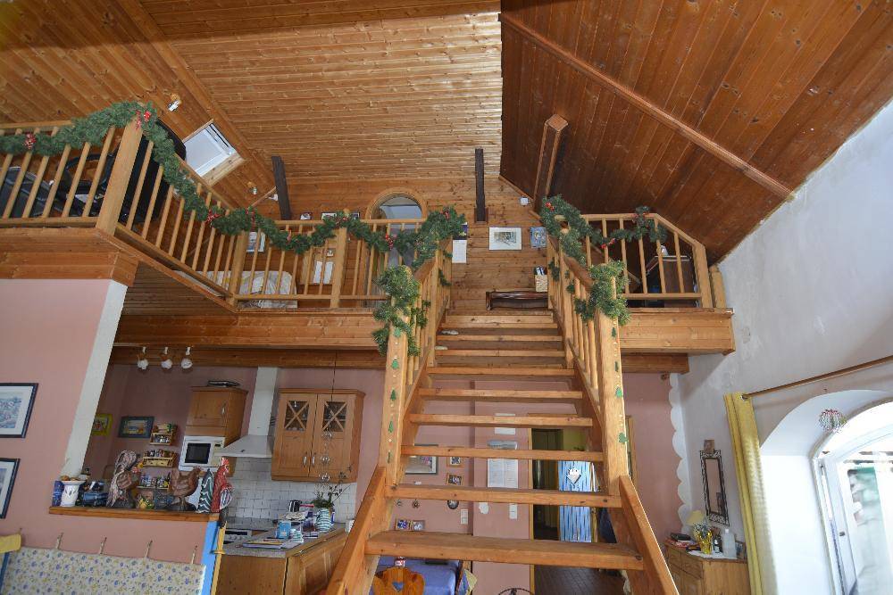 Offener Wohnbereich mit Holztreppe, Galerie und sichtbarer Küche im Hintergrund.