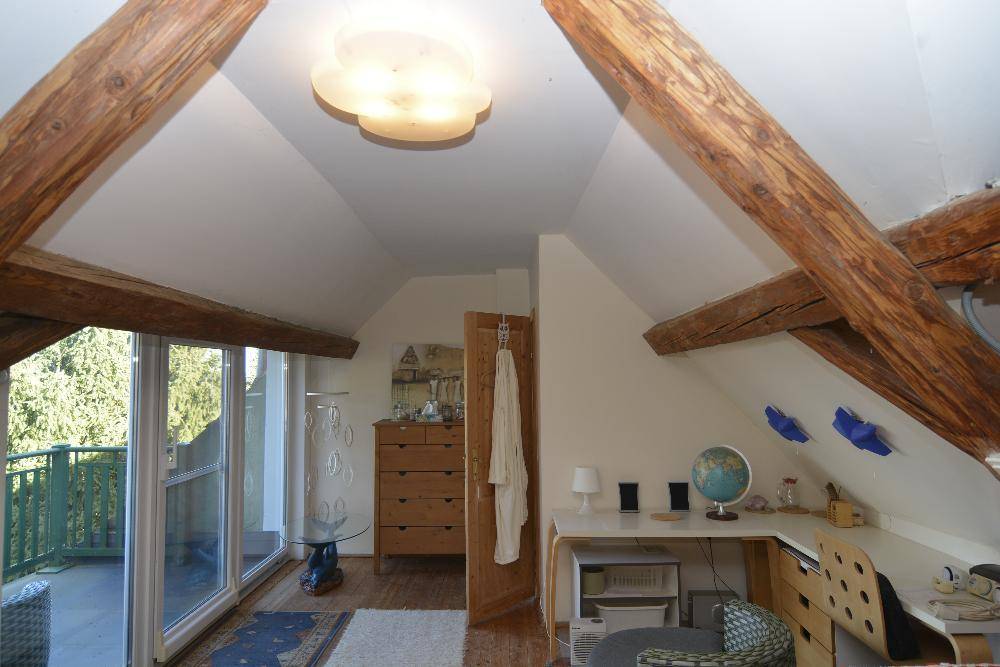 Arbeitsbereich im Dachgeschoss mit Holzbalken, Schreibtisch und Zugang zum Balkon.