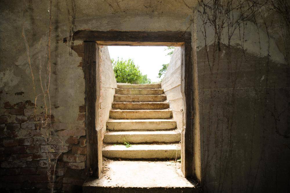 Steintreppe führt aus dem Keller ins Freie, umgeben von alten Ziegelwänden.
