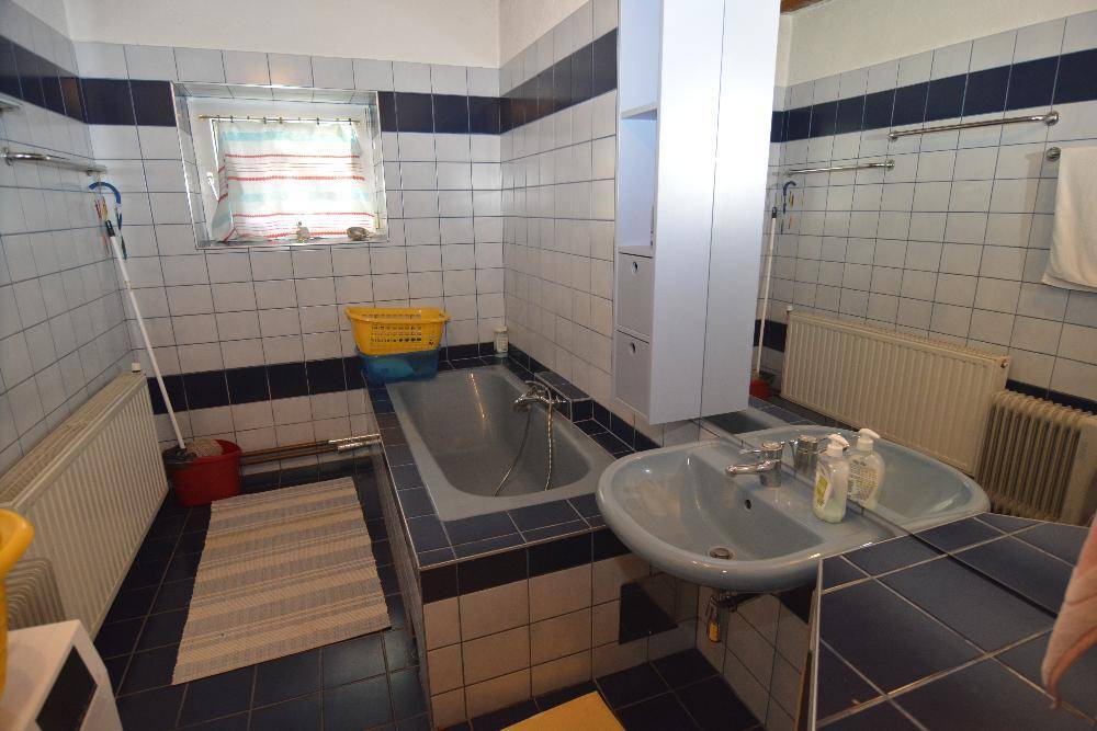 Badezimmer mit Badewanne, Waschbecken und blauen Fliesen im 80er-Jahre-Stil.