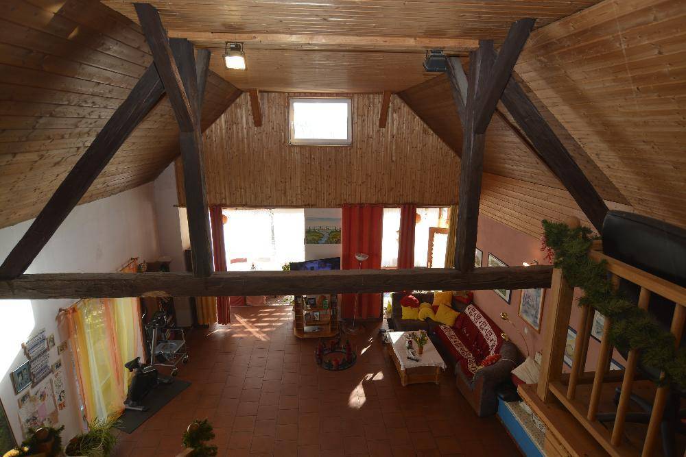 Geräumiger Wohnbereich mit hohen Decken, Holzbalken und Blick auf die untere Ebene.