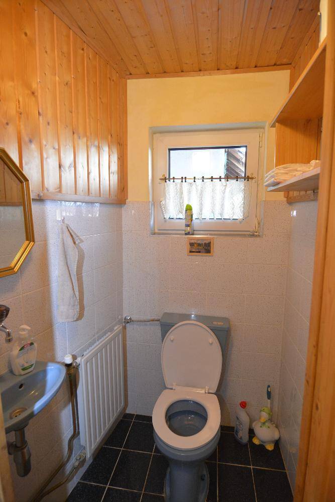 Kleines WC mit Fenster, Waschbecken und Holzvertäfelung an der Decke.