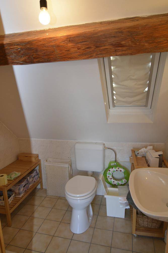 Kleines WC im Dachgeschoss mit Dachfenster, Holzbalken und Fliesenboden.