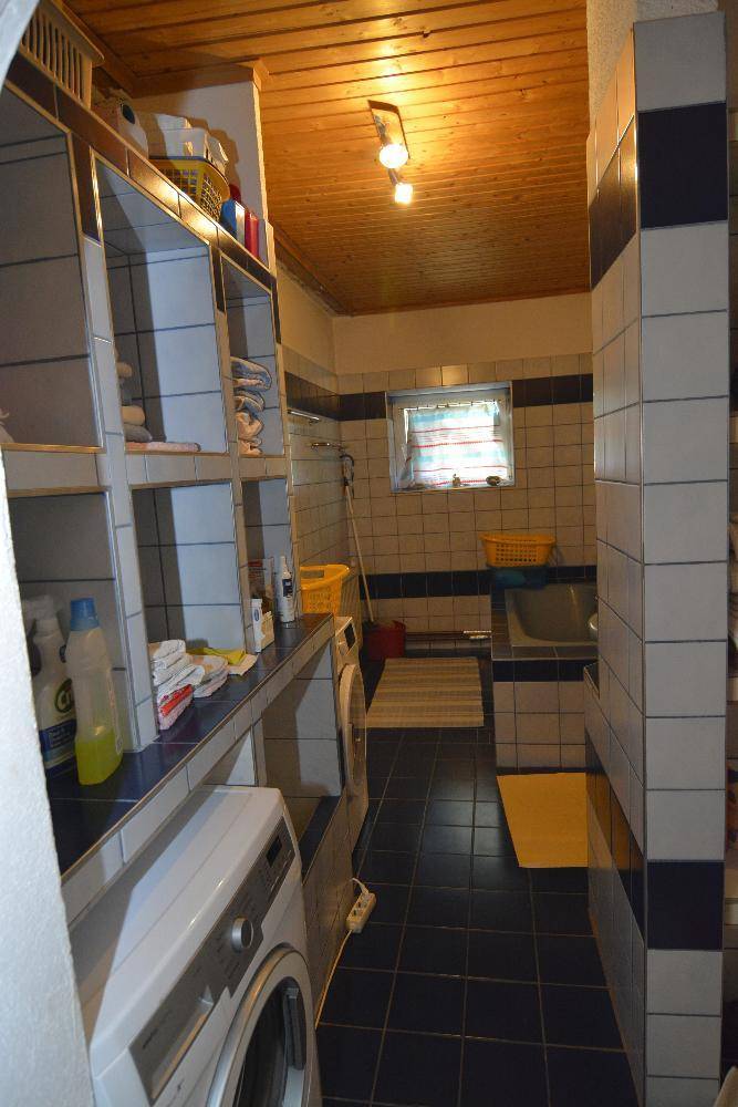 Badezimmer mit Waschmaschine, blauen Fliesen und Holzdecke im 80er-Jahre-Stil.