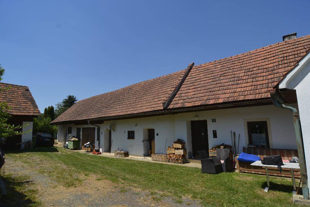 Ländliches Anwesen mit mehreren Gebäuden, Holzlager und Gartenmöbeln im Freien.