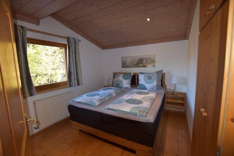 Gemütliches Schlafzimmer mit Doppelbett, Holzboden und Holzdecke, hell durch das Fenster.