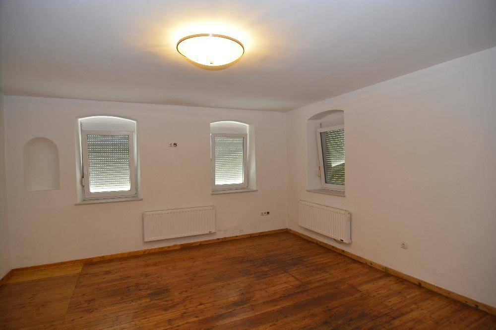 Geräumiges Zimmer mit Holzdielenboden, mehreren Fenstern und Heizkörpern.