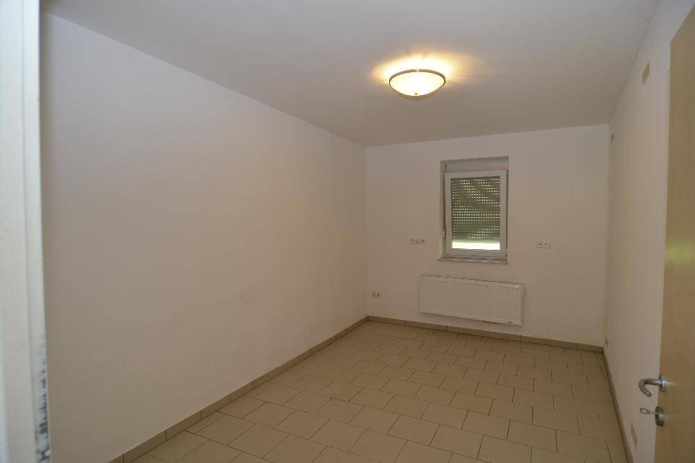 Kleineres Zimmer mit hellen Fliesen, einem Fenster und Heizkörper an der Wand.