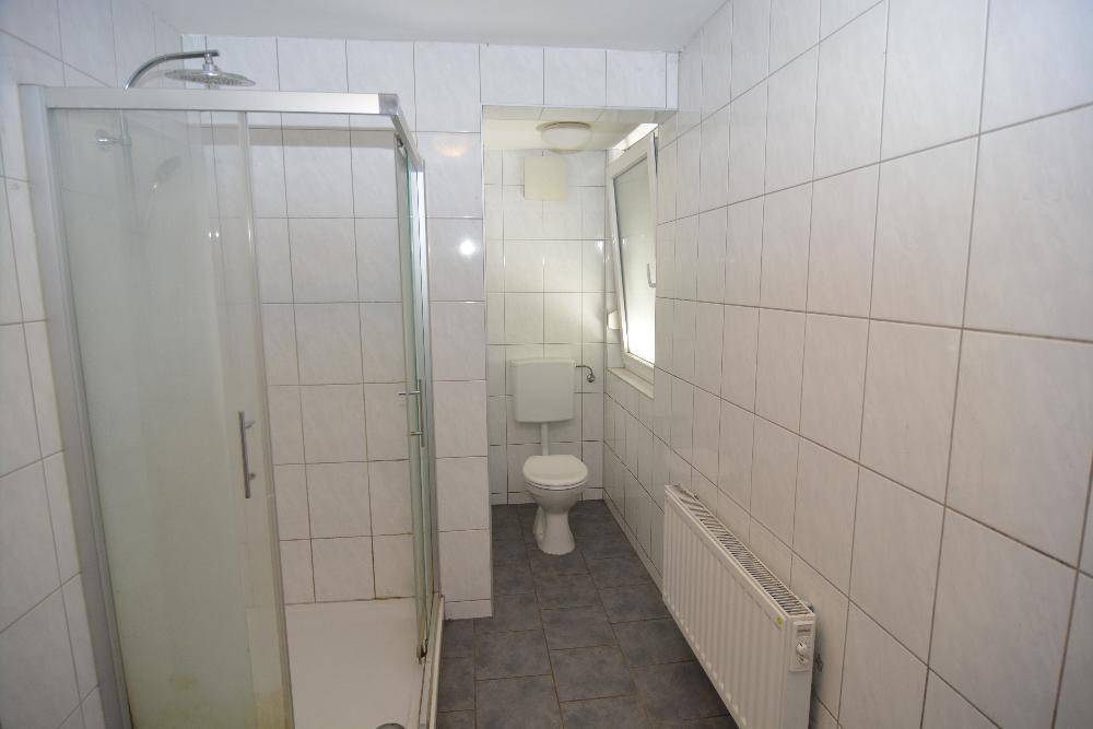 Helles Badezimmer mit Duschkabine, Toilette, Fenster und Fliesen an Wänden und Boden.