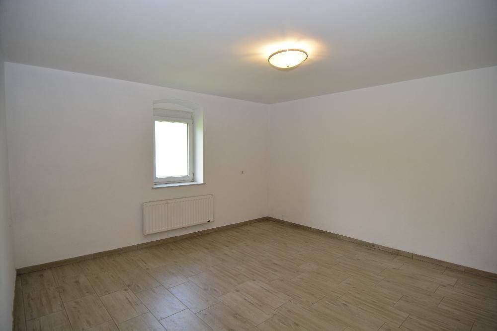 Leeres Zimmer mit hellem Fliesenboden, Fenster und Heizkörper an der Wand.