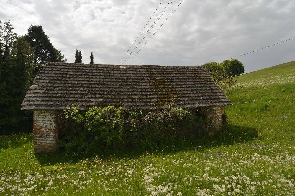 Altes Ziegelgebäude mit moosbewachsenem Ziegeldach und umgebender grüner Wiese.