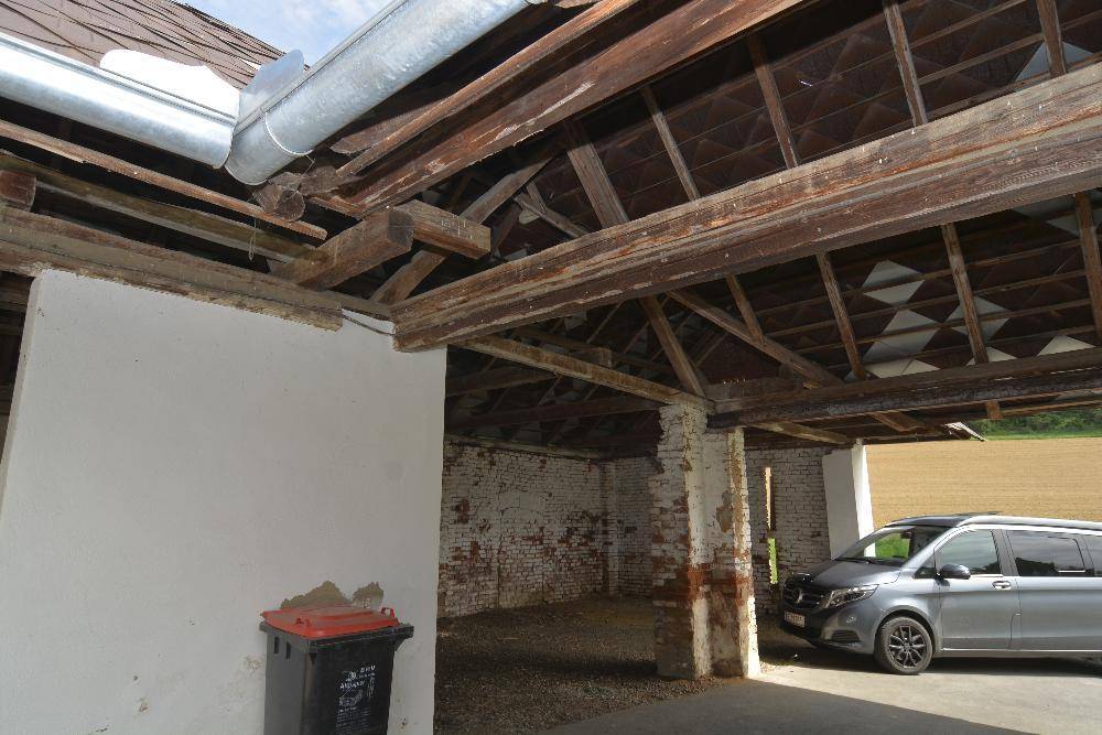 Offene Scheunenstruktur mit freiliegenden Holzbalken und Blick auf ein geparktes Auto.