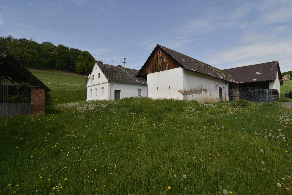 Mehrere ländliche Gebäude mit Scheunendächern inmitten einer weiten grünen Wiese.