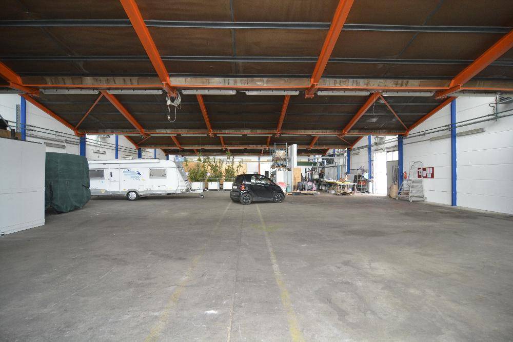 Geräumiger Lagerraum mit Betonboden, sichtbaren Stahlträgern und einem geparkten Wohnwagen.