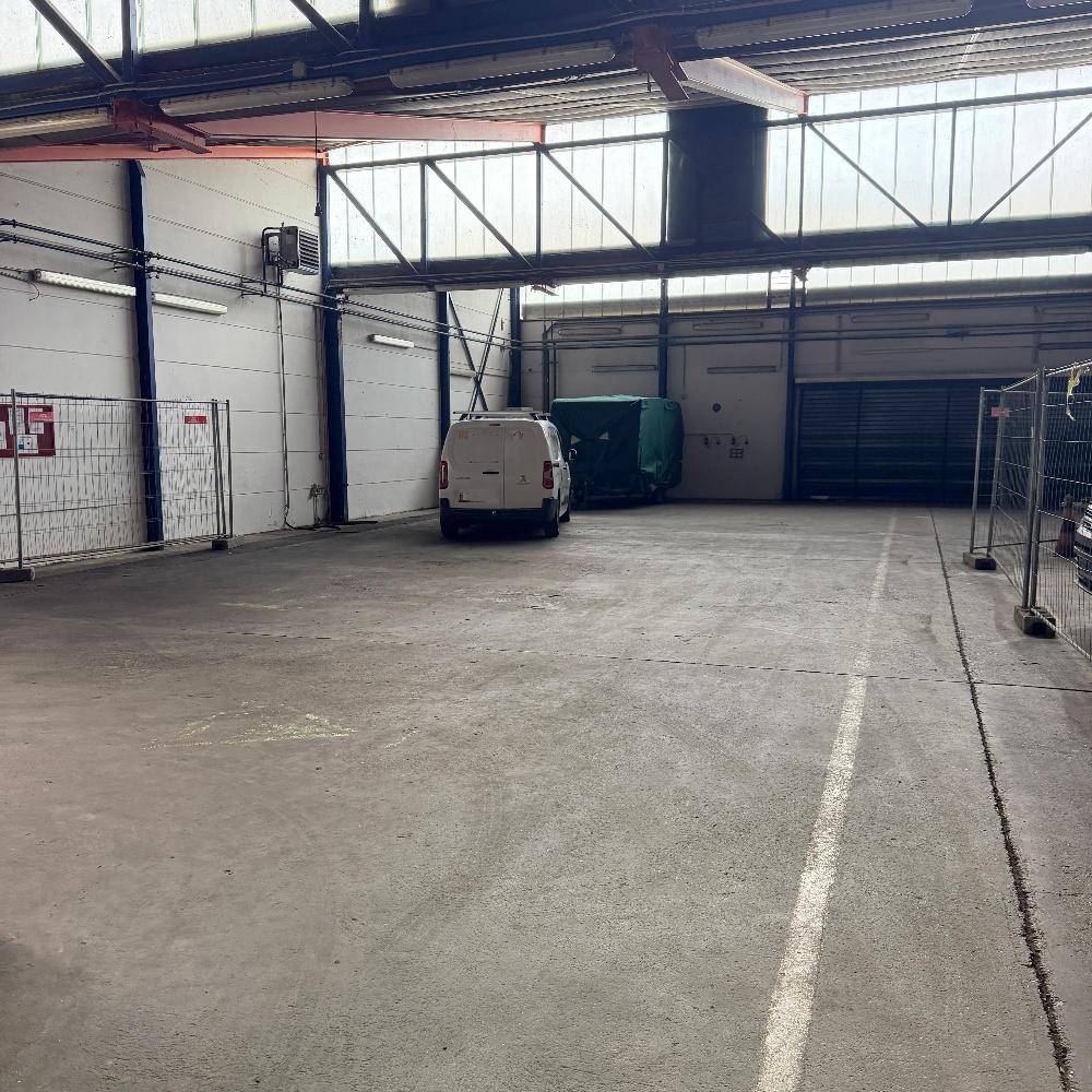Großer, leerer Lagerraum mit Betonboden, hohen Decken und einem geparkten Lieferwagen.