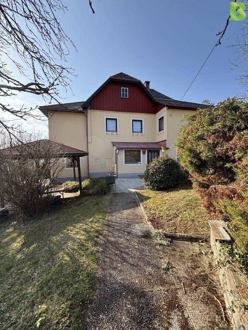 Vorderansicht des Hauses mit gelber Fassade, rotem Dach und einem gepflasterten Weg.