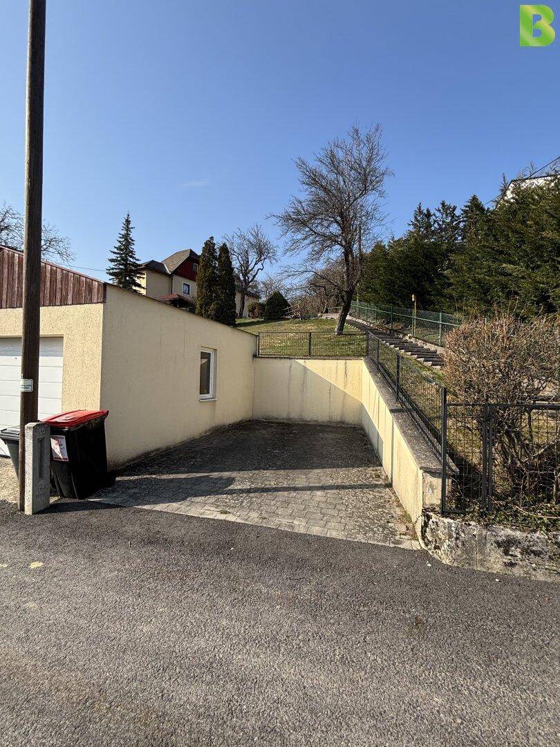 Außenparkplatz oder Zufahrt mit Garage und Treppenaufgang zum oberen Grundstücksbereich.