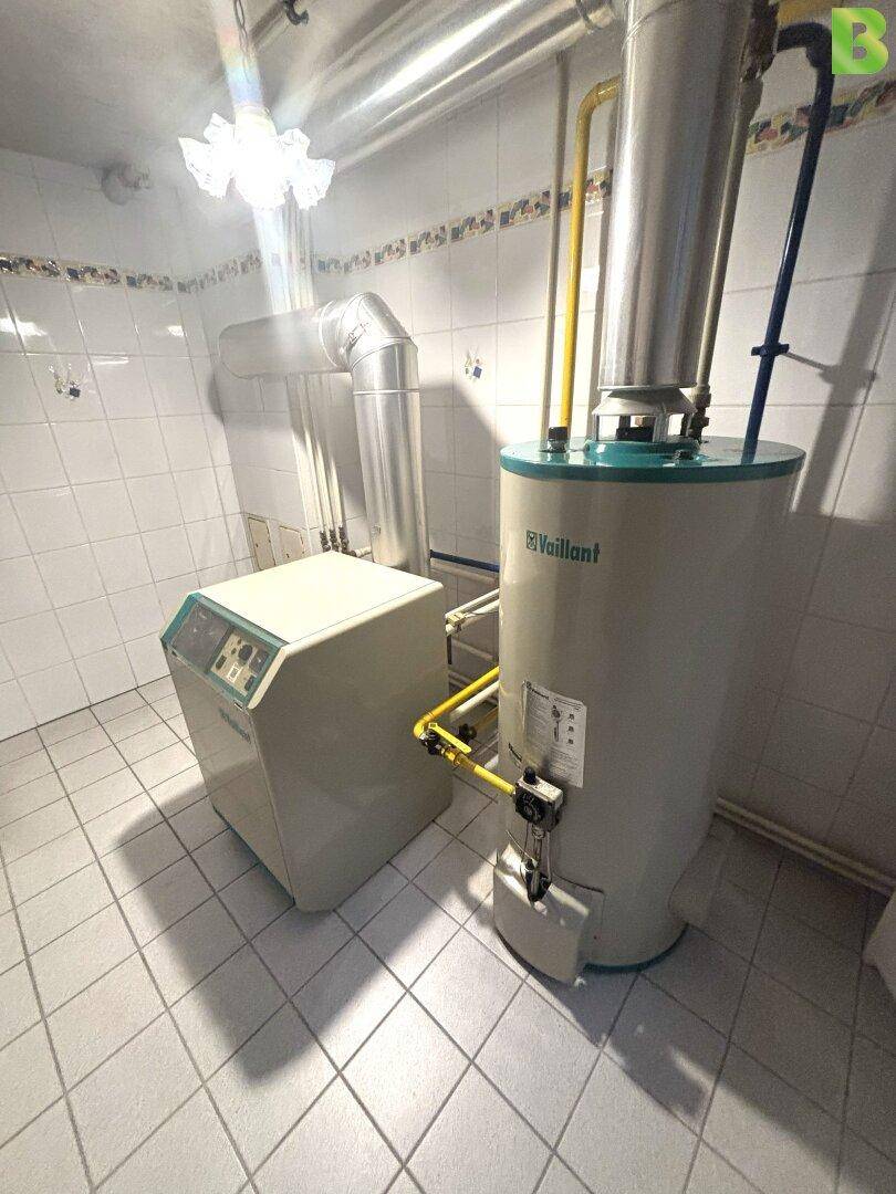 Heizungsraum mit Gastherme und Warmwasserspeicher, umgeben von weißen Fliesen.