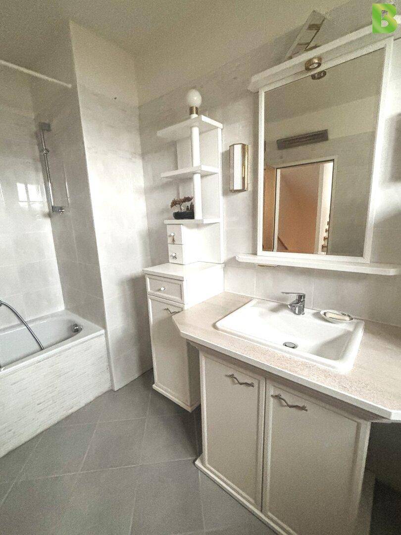 Helles Badezimmer mit Badewanne, Einzelwaschbecken und großem Spiegel.
