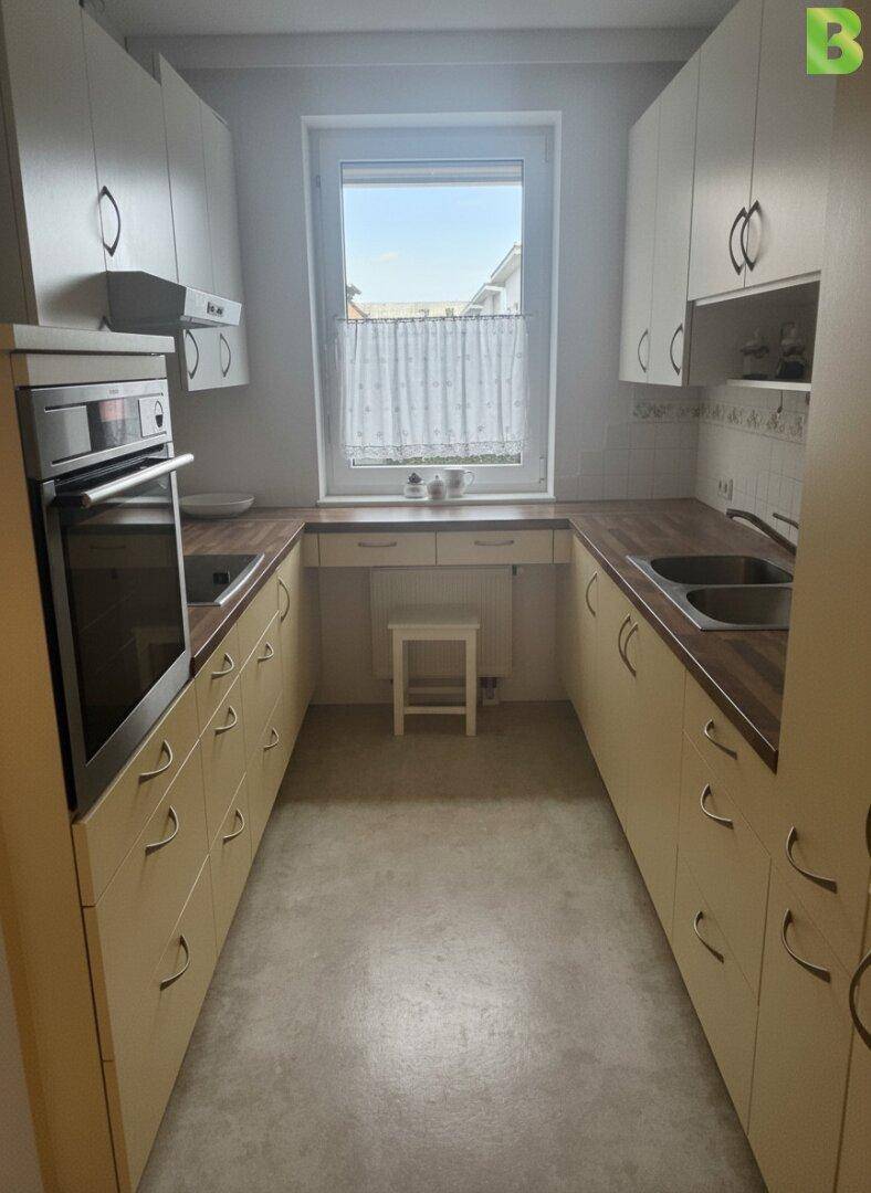 Funktionale Küche mit beigen Schränken, Holz-Arbeitsplatten und Fenster für Tageslicht.
