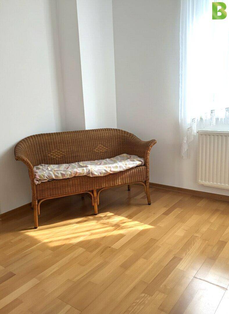 Heller Raum mit Korbbank, Parkettboden und großem Fenster mit viel Tageslicht.