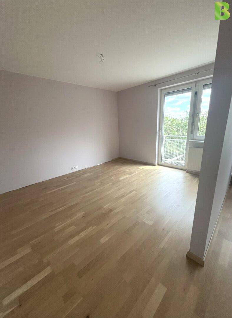 Leeres Zimmer mit hellem Parkettboden und Zugang zu einem französischen Balkon.