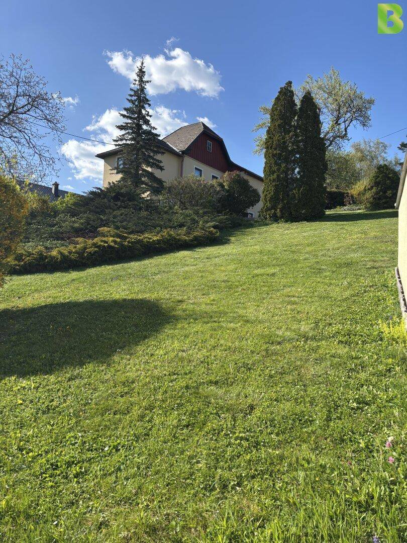 Hanglage mit gepflegtem Rasen und einem traditionellen Haus im Hintergrund.