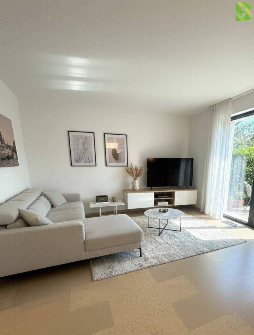 Helles Wohnzimmer mit modernem Sofa, TV-Möbel und großem Fenster mit Zugang zum Außenbereich.
