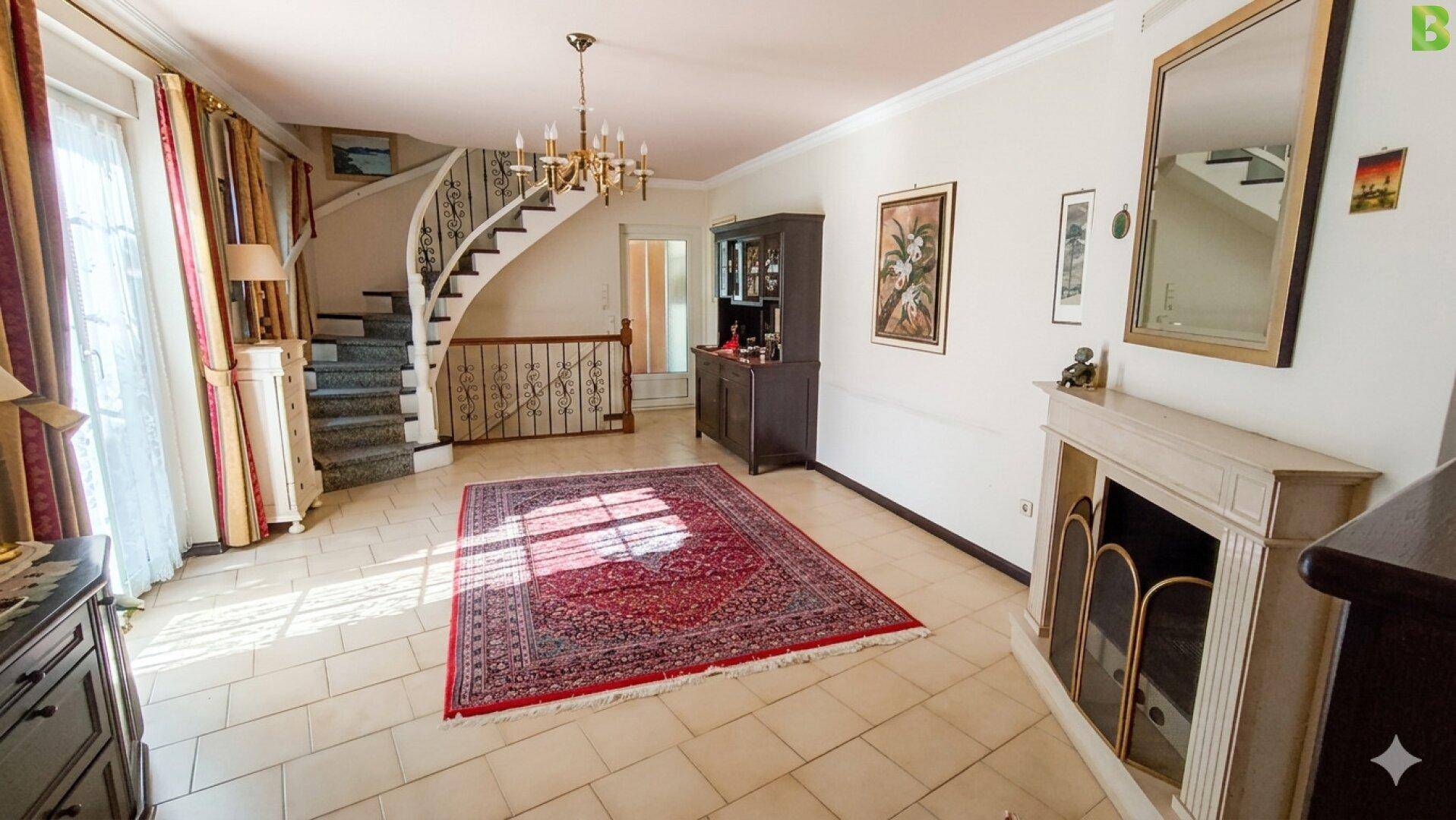 Elegantes Wohnzimmer mit geschwungener Treppe, Kamin und Fliesenboden.