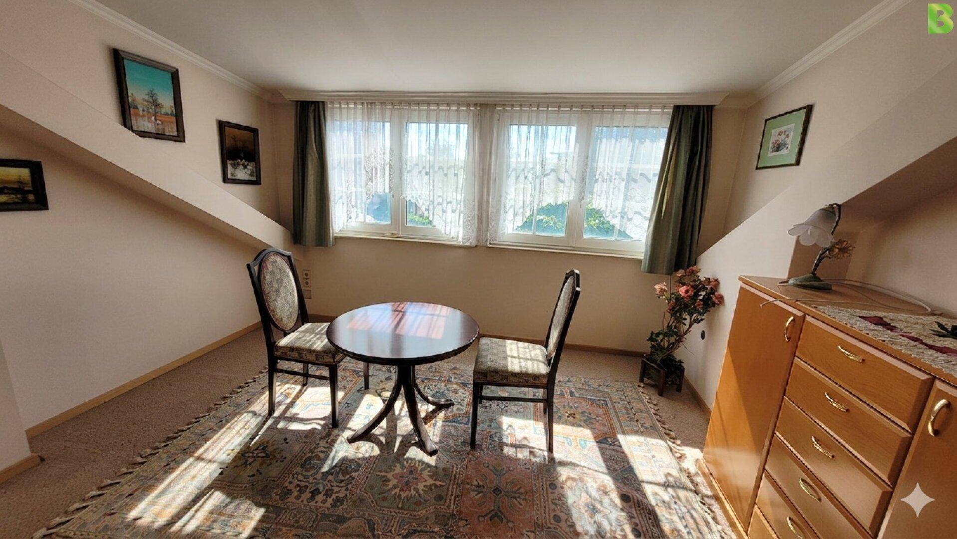 Gemütliches Zimmer im Dachgeschoss mit schrägen Wänden und Teppichboden.