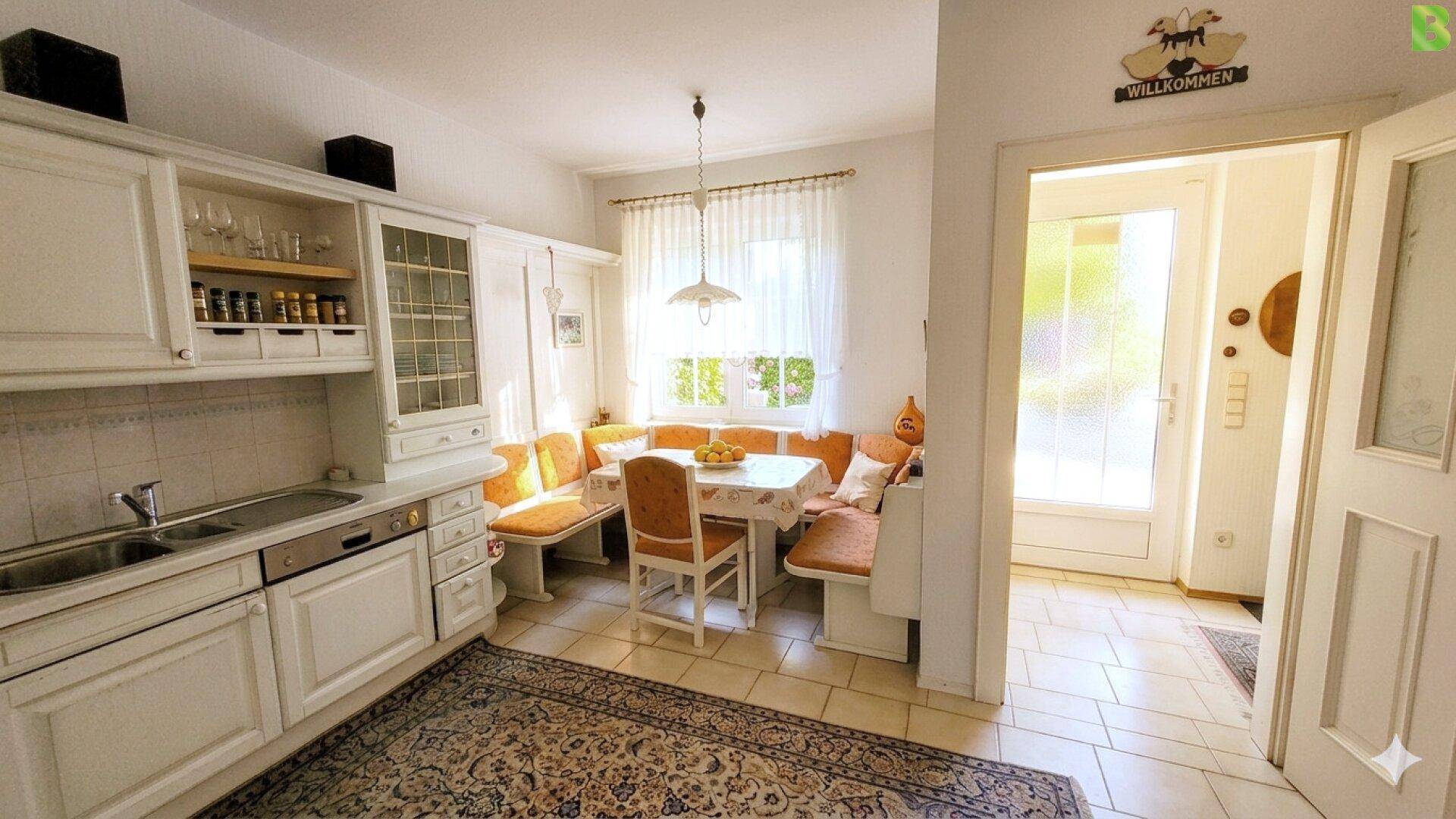 Gemütliche Küche mit Essecke, weißen Schränken und Zugang zum Flur.
