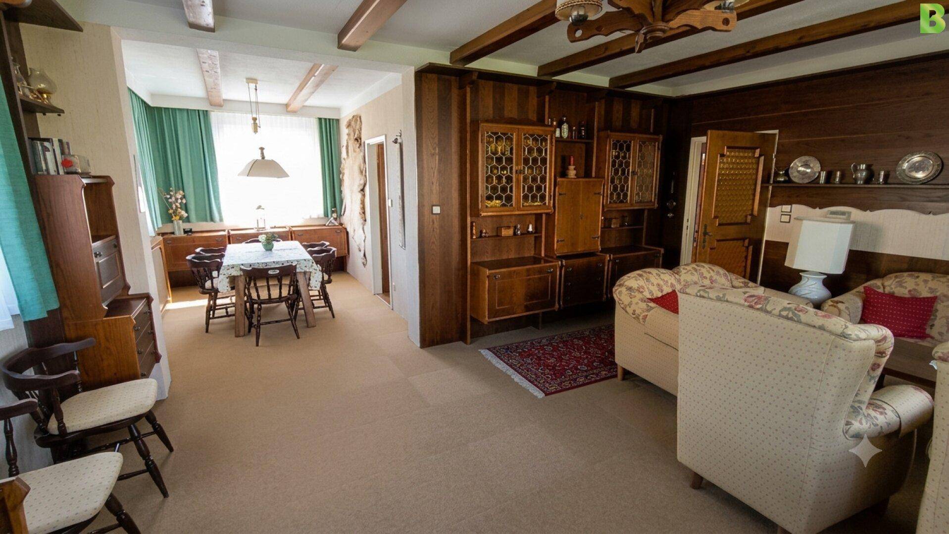 Geräumiger Wohn- und Essbereich im Landhausstil mit Holzbalken und Teppichboden.